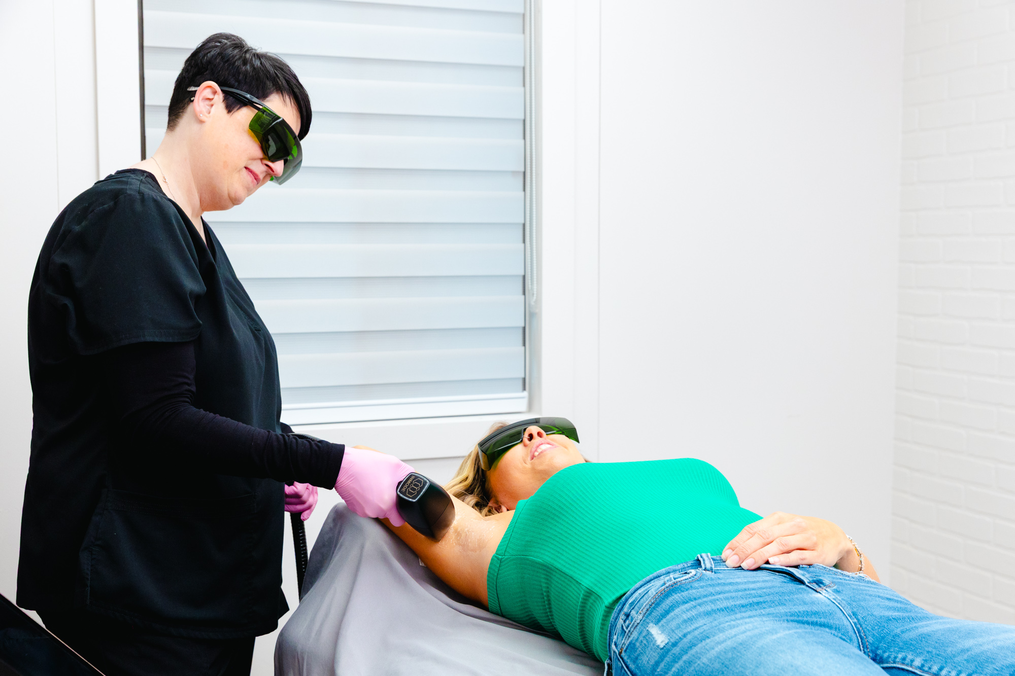 A provider carefully guides the handheld treatment device over a patient's underarm area during her laser hair removal in Columbus. They both wear special protective eyewear during the treatment.